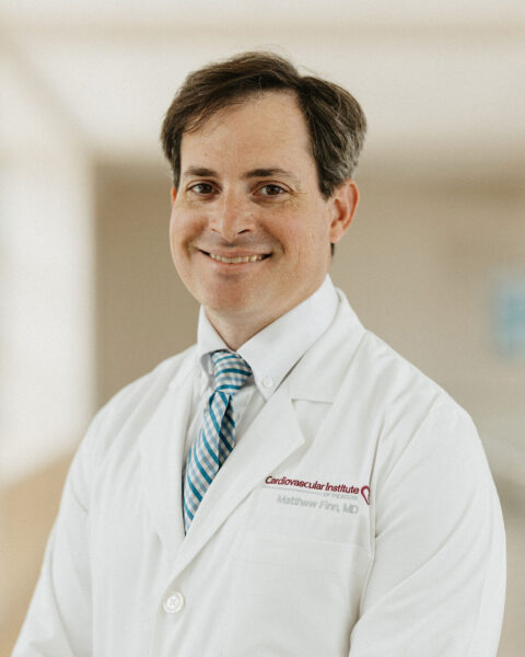 Professional cardiologist in a white lab coat with a stethoscope, confidently smiling.