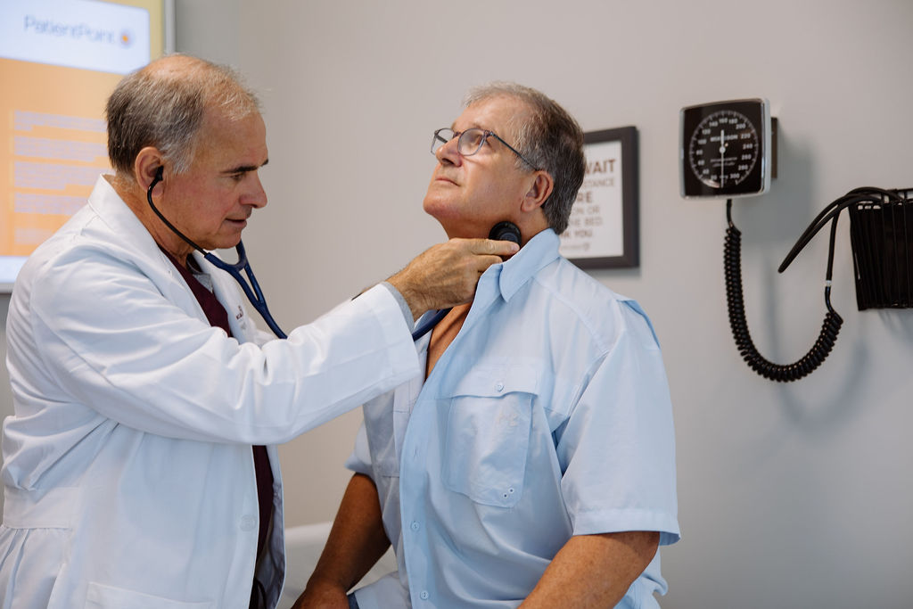 A doctor uses a stethoscope to examine an older man seated in a medical office.