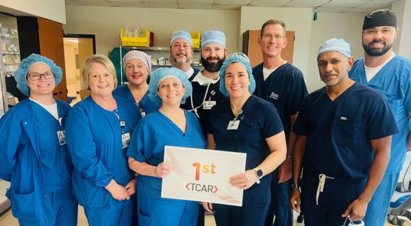 A group of medical professionals in scrubs pose indoors, celebrating the 1st TCAR for carotid artery disease in New Iberia.